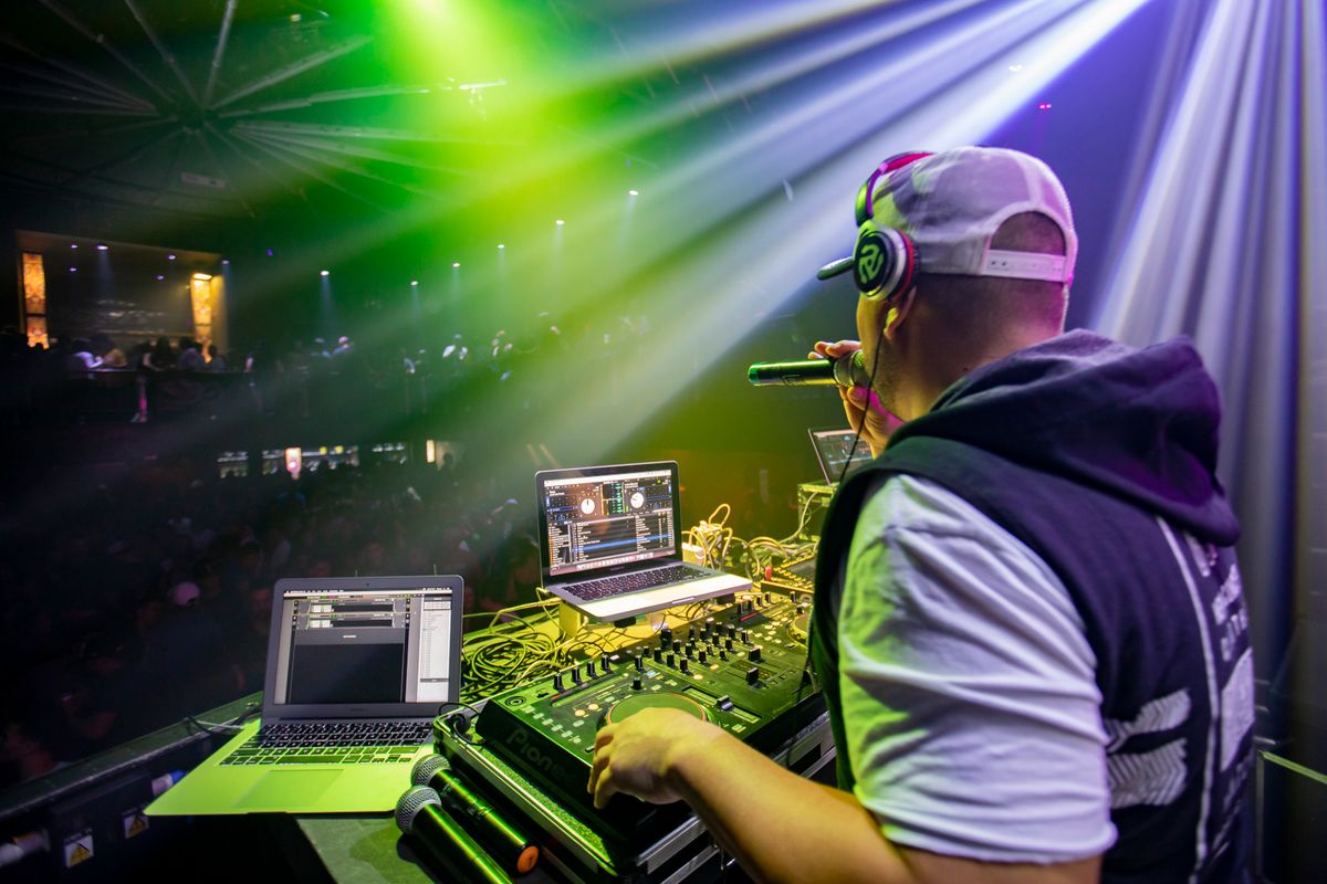 DJ operando la consola en un evento con luces verdes y violetas